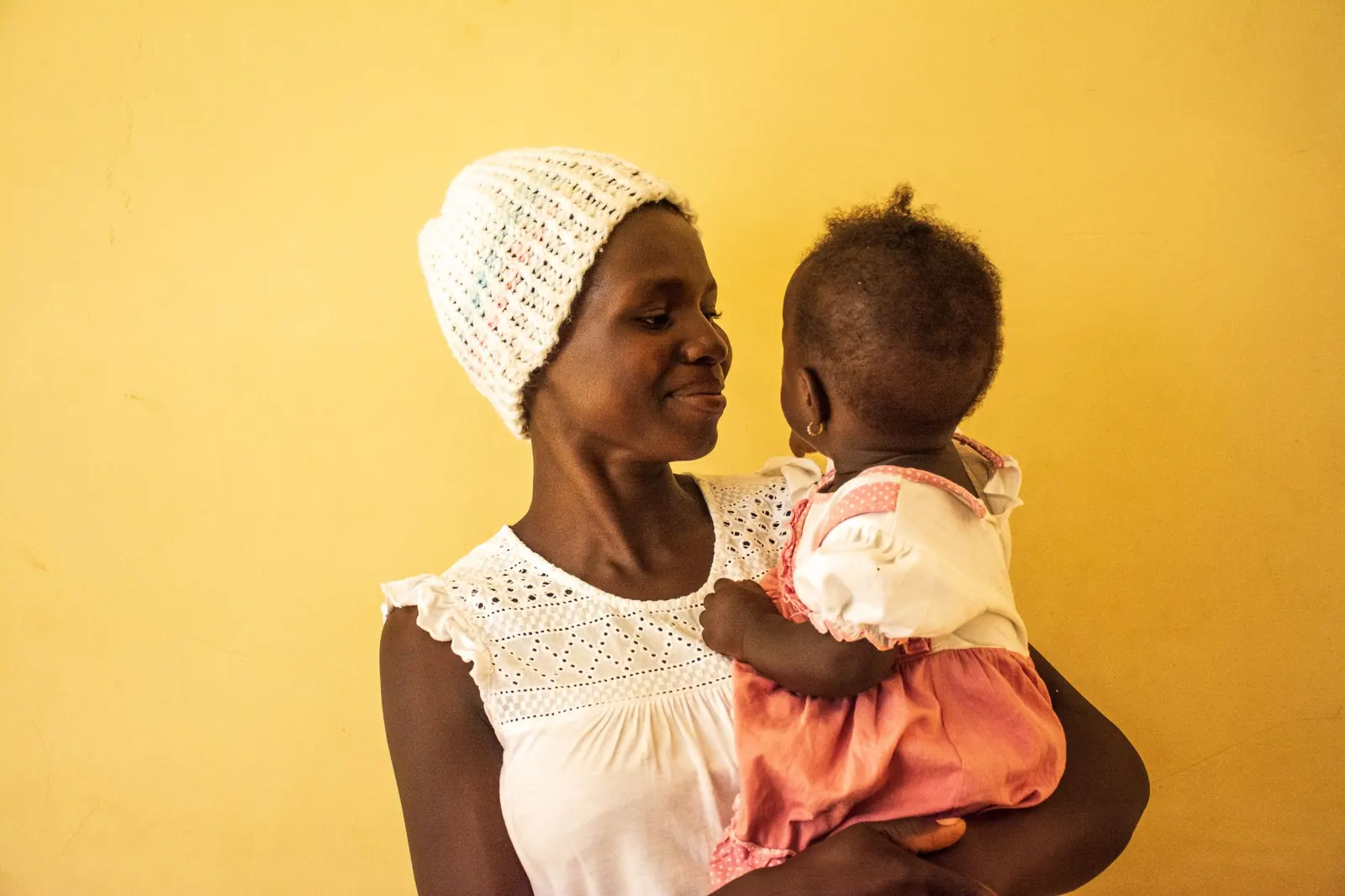 Mother smiling at her baby daughter against a warm yellow wall